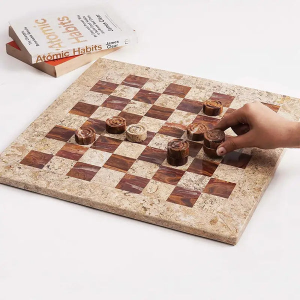 Hand placing red marble checkers disc mid-game — coral and red marble checkers set 15 inch with books and candle by RADICALn