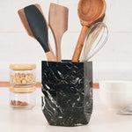 Faceted black marble utensil holder on a white kitchen countertop with wooden spoons and whisk