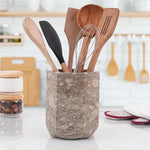 Faceted oceanic marble utensil holder on a white kitchen countertop with wooden spoons and whisk