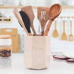 Faceted verona marble utensil holder on a white kitchen countertop with wooden spoons and whisk