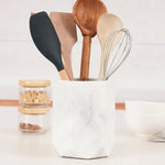 Faceted white marble utensil holder on a white kitchen countertop with wooden spoons and whisk