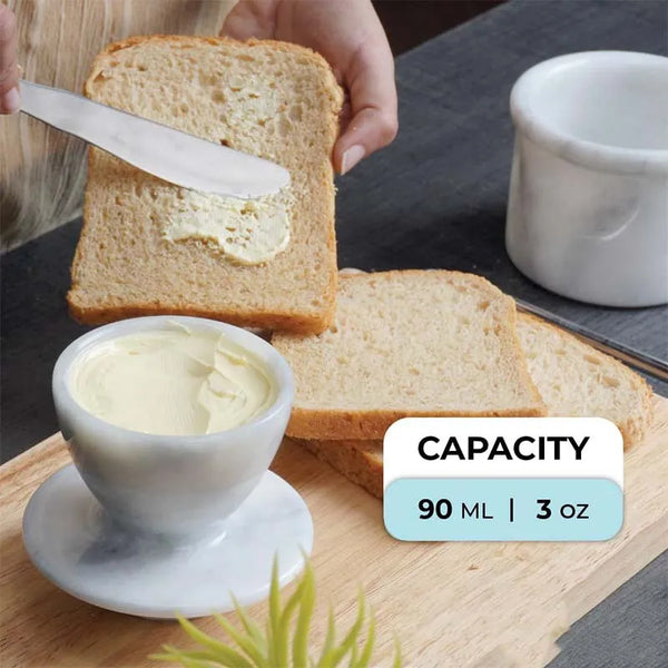 Soft butter from a 3 oz white marble butter keeper being spread on toast with a knife