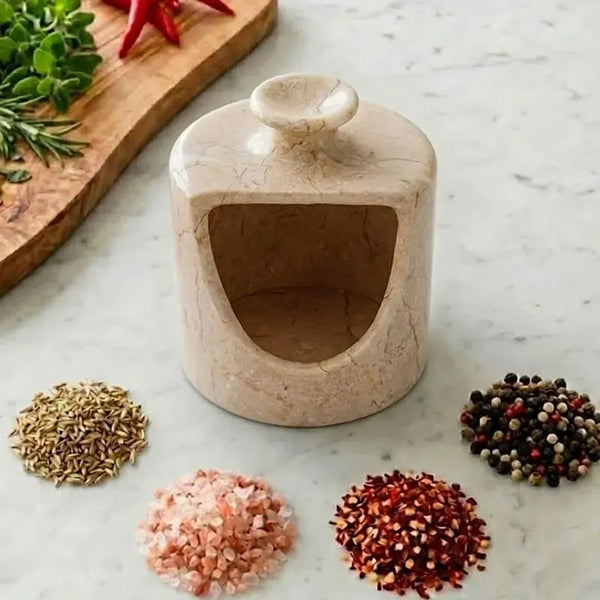 Verona marble salt pig with an open front cut-out, surrounded by piles of pink salt, chilli flakes, cumin and peppercorns