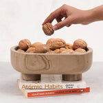Natural brown marble trinket bowl on books, filled with walnuts, hand reaching in