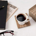 Natural brown square marble coaster under a white coffee cup beside a newspaper and glasses