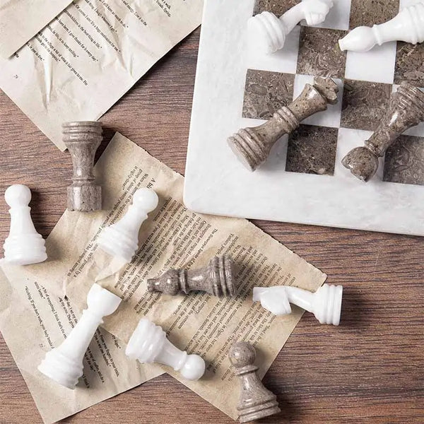 Oceanic grey and white marble chess pieces scattered on book pages — board corner detail by RADICALn
