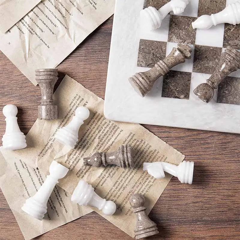 Oceanic grey and white marble chess pieces scattered on book pages — board corner detail by RADICALn