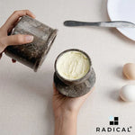 Hands lifting the crock base off an oceanic marble butter keeper to reveal butter packed in the lid