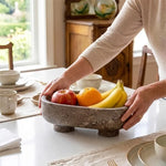 Hands placing fruit into an oceanic marble footed bowl on a kitchen counter