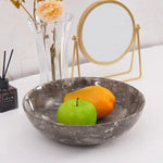 Oceanic marble fruit bowl holding a green apple and a mango on a console table beside a vase and mirror
