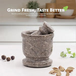 Oceanic marble mortar and pestle on a kitchen counter with whole peppercorns, cardamom pods and fresh coriander
