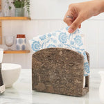 Hand pulling a floral napkin from a oceanic marble napkin holder in a kitchen