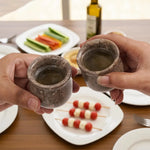 Two hands toasting with oceanic marble shot glasses over a table of appetizers