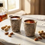 Two oceanic marble shot glasses of whiskey on a rustic table with cards and nuts