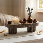Oceanic footed marble tray holding a candle, reed diffuser and pinecones on a bedside table