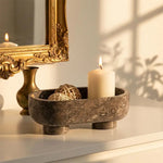 Oceanic marble footed bowl holding a candle and rattan balls by a gold mirror