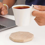 Travertine octagon coaster on a desk as a hand lifts a mug of tea beside a laptop