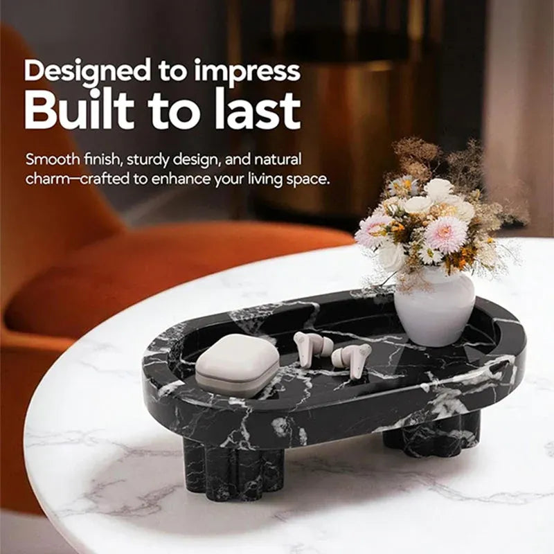 Raised black marble tray on fluted legs holding earbuds and a vase on a side table