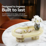 Raised green onyx marble tray on fluted legs holding earbuds and a vase on a side table