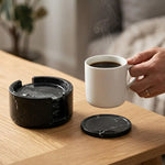 Hand lifting a tea cup from a round black marble coaster beside its matching stone holder