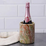 Round green onyx marble wine cooler chilling a sparkling bottle beside a linen towel on dark wood