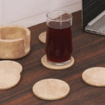 Round verona marble coasters and holder on a dark wood desk with a glass of iced tea beside a laptop