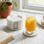 Round white marble coaster set with holder beside a glass of orange juice on a linen cloth