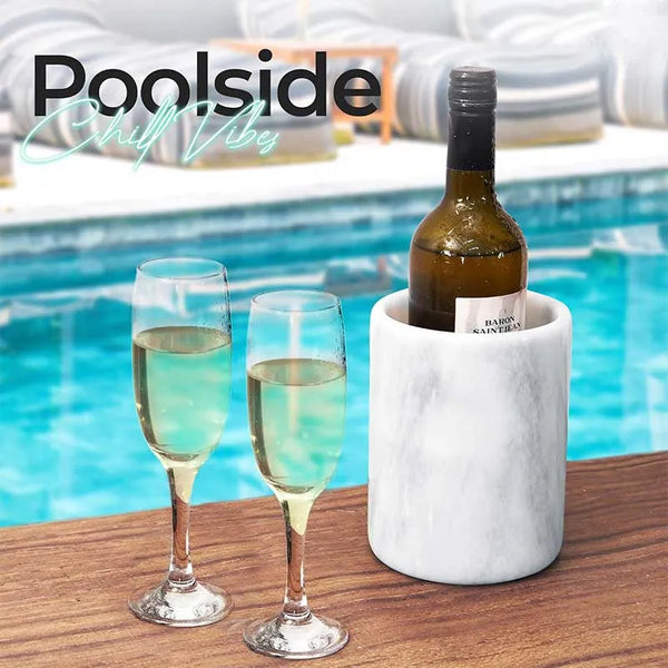 Round white marble wine cooler chilling a bottle beside two champagne flutes poolside