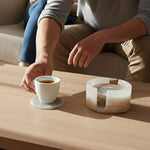 Hand lifting a tea cup from a round white onyx marble coaster beside its matching stone holder