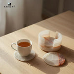 Round white onyx marble coaster set with holder beside a tea cup on a wooden table