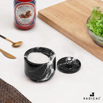 Small black marble seasoning keeper filled with salt, stainless steel knob lid set to the side on a countertop