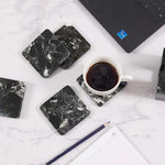 Square black marble coasters on a white desk with a laptop, notepad and cup of coffee