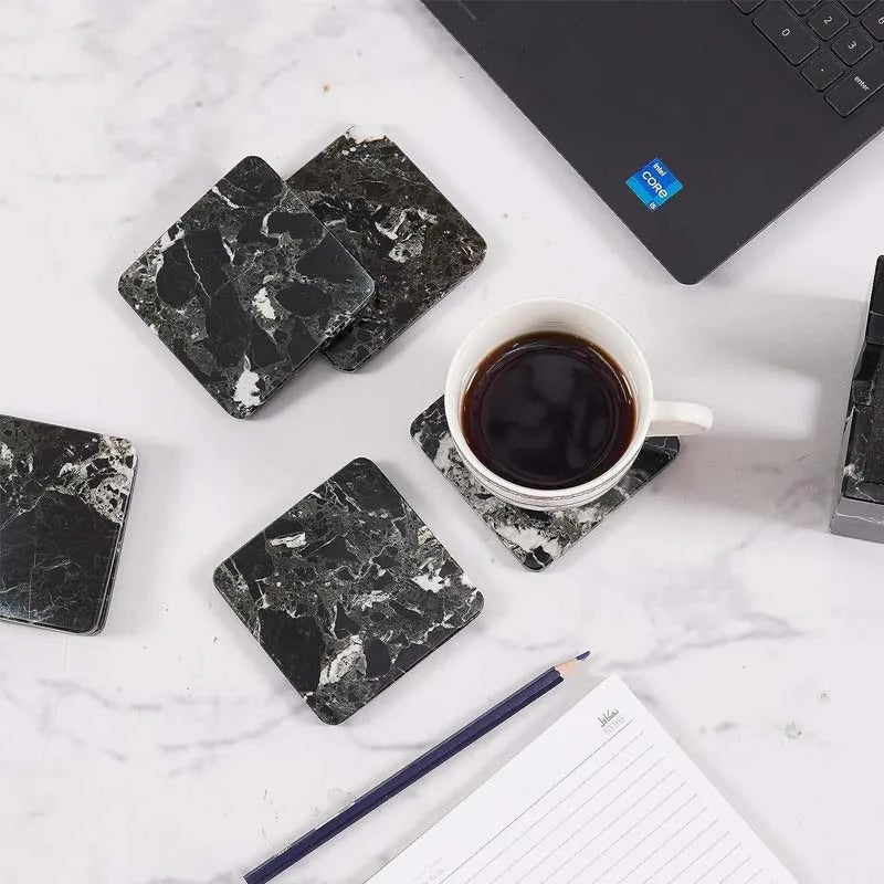 Square black marble coasters on a white desk with a laptop, notepad and cup of coffee