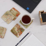 Square green onyx marble coasters on a white desk with a laptop, notepad and cup of coffee