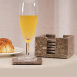 Stack of square oceanic marble coasters beside a champagne flute and croissant