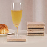 Stacked square travertine coasters beside a champagne flute and croissant