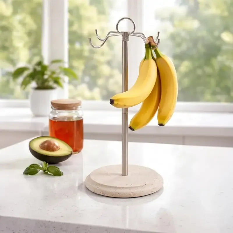 Travertine marble banana holder on a kitchen counter holding a bunch of bananas, with avocado and honey nearby
