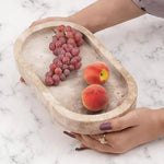 Hands holding a travertine footed marble bowl with grapes and a peach