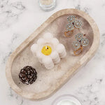 Travertine marble oval tray holding a candle, earrings and a pinecone on marble