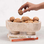 Travertine marble trinket bowl on books, filled with walnuts, hand reaching in