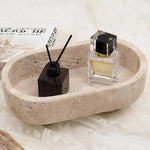 Travertine oval marble trinket dish holding a reed diffuser and perfume beside books