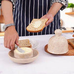 Butter being spread on toast with the marble knife from a verona marble butter dish, dome lid resting on a wooden board