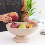 Hand placing an apple into a verona marble pedestal fruit bowl holding pomegranate, pear and banana