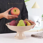 Hand placing an apple into a verona marble pedestal fruit bowl already holding a pear and plums