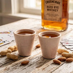 Two verona marble shot glasses of whiskey on a rustic table with cards and nuts