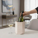 Hand lowering a wine bottle into a verona hexagon marble wine cooler on a table