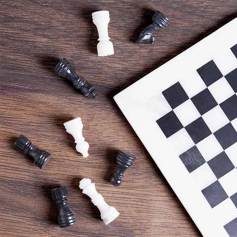 White and black marble chess set 12 inch — pieces scattered on dark wood surface showing white marble and black stone detail by RADICALn