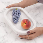Hands holding a white footed marble bowl with grapes and a peach