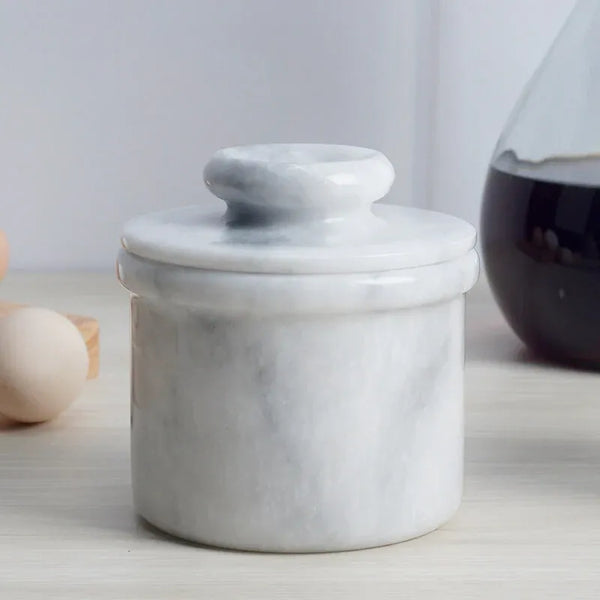 Handmade white marble butter keeper with domed lid on a kitchen counter beside eggs
