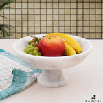 White marble footed fruit bowl on a pedestal base holding an apple, bananas and grapes